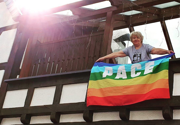 Jemand hängt eine Regenbogenflagge mit der Aufschrift 'Pace' vom Balkon 